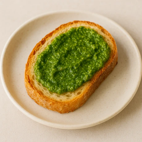Kromka chleba z zielonym pesto z ziół na ceramicznym talerzu