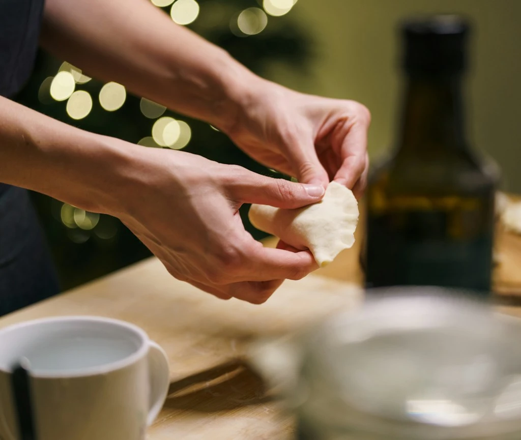Dłonie sklejające brzegi pieroga podczas ręcznego lepienia pierogów wigilijnych.