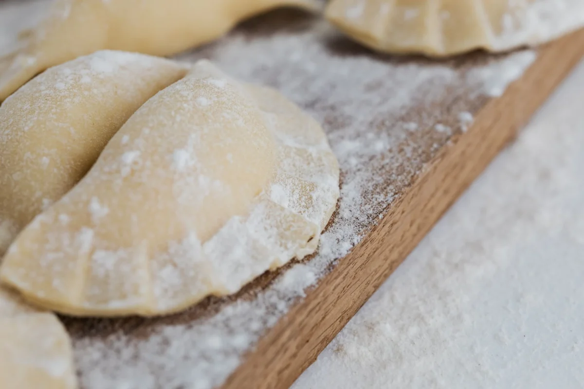 Surowe domowe pierogi wigilijne oprószone mąką, ułożone na drewnianej stolnicy.